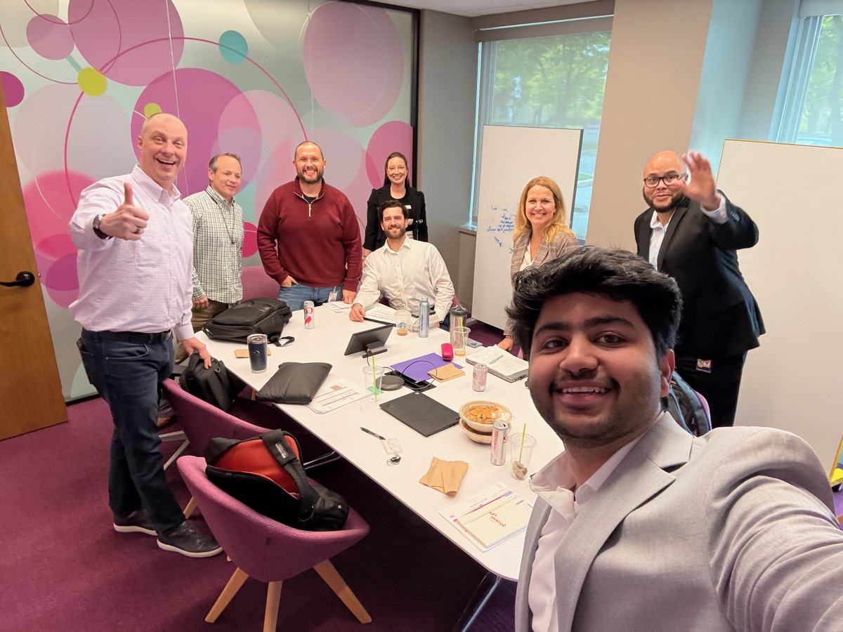 Mohit and a client program team gathered around a workshop table, smiling after a working session